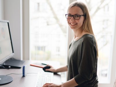 Studentin steht am Schreibtisch und arbeitet am PC.