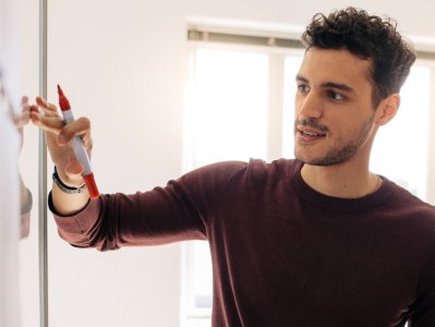 Student steht mit Stift in der Hand an einem Whitboard.