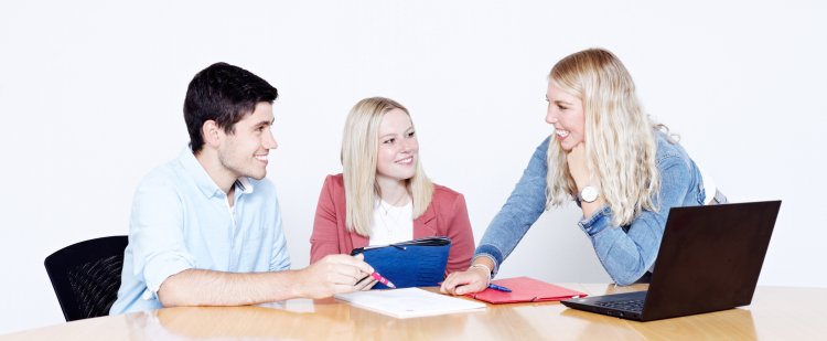 Gruppe von Nachwuchskräften am Tisch mit Laptop und Mappen.