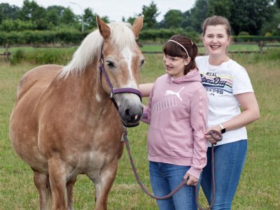 Auszubildende und Klientin stehen auf der Weide neben einem Pferd.