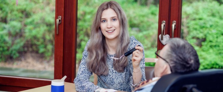 Praktikantin füttert Klient im Rollstuhl mit Joghurt.