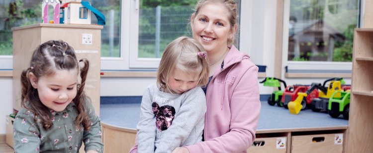 Erzieherin und zwei Mädchen mit Spielzeug im Kindergarten.