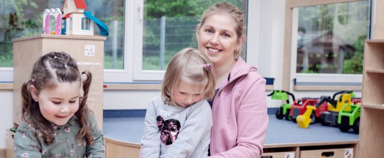 Junge Frau spielt mit zwei Kindern auf dem Boden.