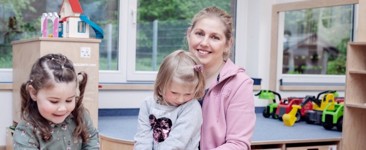 Praktikantin und zwei Mädchen mit Spielzeug im Kindergarten.