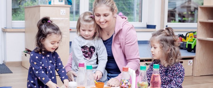 Praktikantin und drei Mädchen mit Spielzeug im Kindergarten.