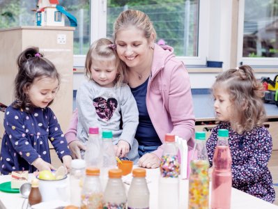 Praktikantin und drei Mädchen mit Spielzeug im Kindergarten.