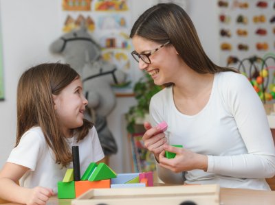 Praktikantin und Mädchen spielen im Kindergarten mit Holzspielzeug.