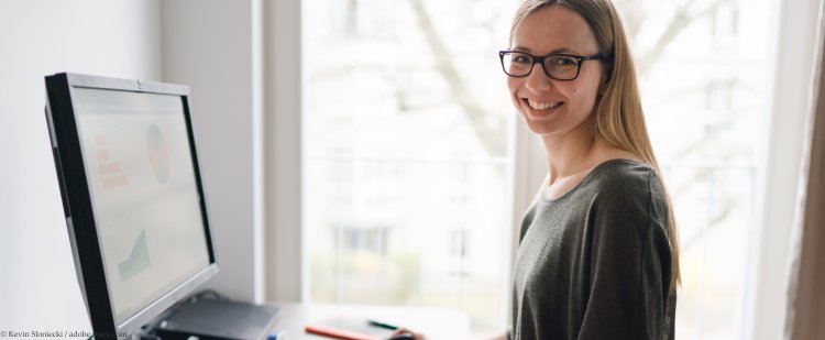 Studentin steht am Schreibtisch und arbeitet am PC.