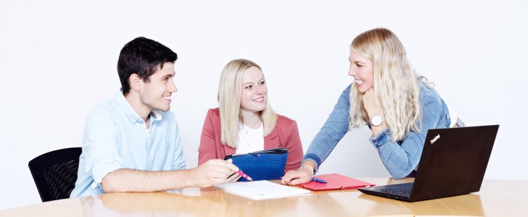 Gruppe von Nachwuchskräften am Tisch mit Laptop und Mappen.